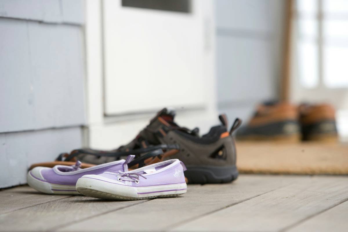 Outdoor contaminants such as pollutants and airborne particulates, always seem to find their way into even the cleanest homes. Keeping a home’s interior free of such irritants, including allergens, dust, and pesticides, means leaving contaminated clothing at the door. In this particular photograph, four pairs of footwear had been left on the front porch so as to not track attached particulates into this house. Note that in this particular instance there is a door matt upon which one can wipe his, or her feet, prior to entering the home.